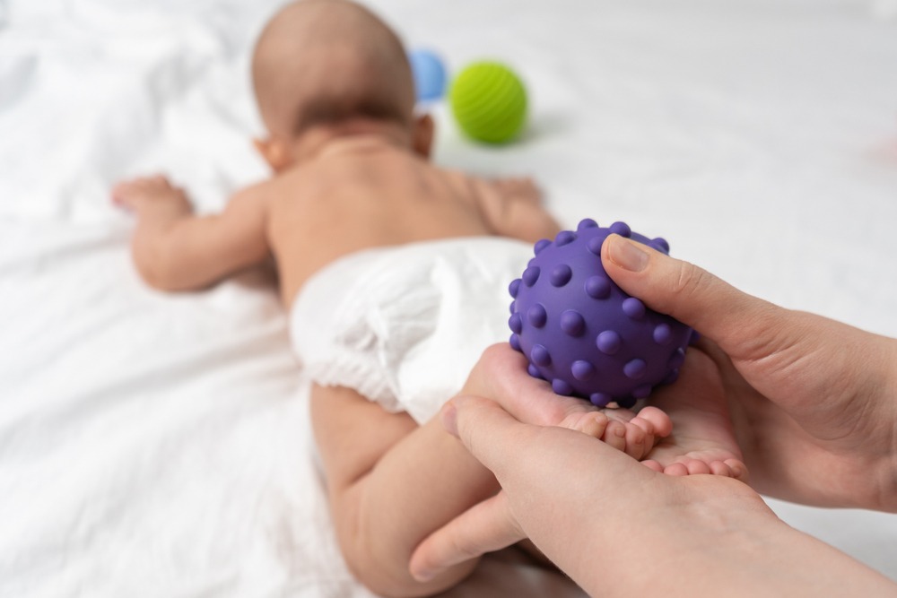 Mom,Massage,The,Baby's,Feet,With,A,Purple,Rubber,Ball.