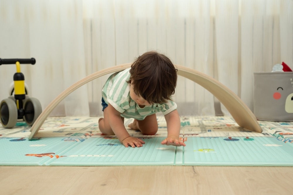 Toddler,Crawling,Under,Balance,Board,In,A,Playroom.